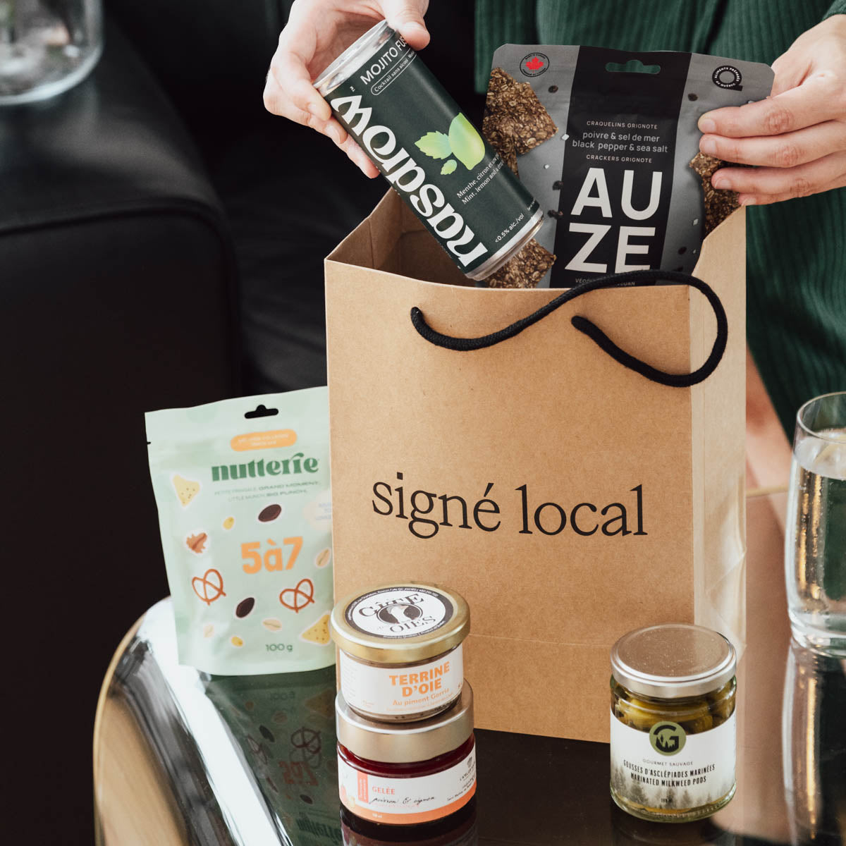 Coffret Apéro Signé Local en situation : mocktail Mojito Nasdrow, craquelins Auze, noix 5 à 7 Nutterie, terrine d'oie, gelée et gousses d'asclépiades autour d'un sac cadeau signé local