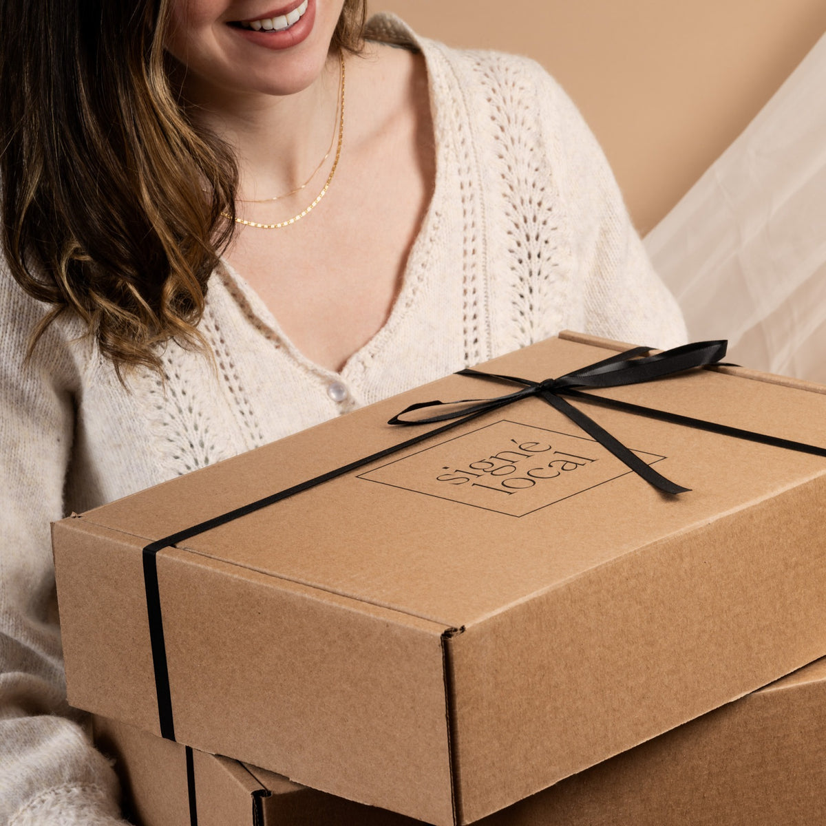 Femme tenant des coffrets cadeaux Signé Local dans leur boîte kraft fermée au ruban noir