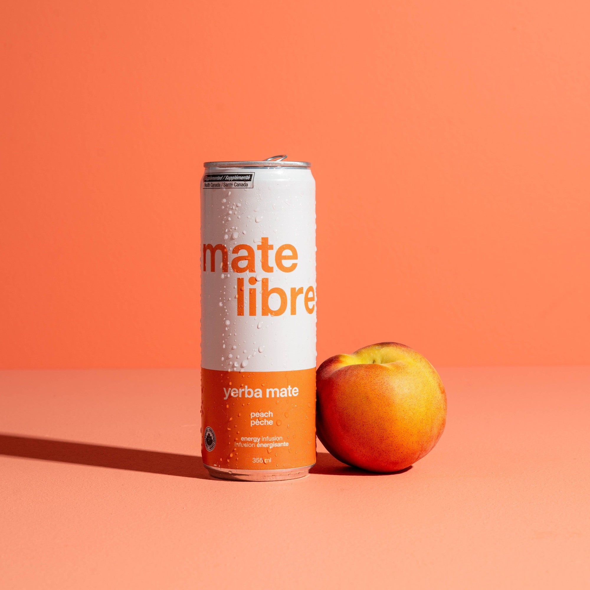 Canette Mate Libre pêche posée à côté d'une pêche fraîche